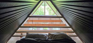 A room with a sloped ceiling, a bed with pillows, and a view of greenery outside. - Views across the fields to the sea on Langeland (Tranekær)