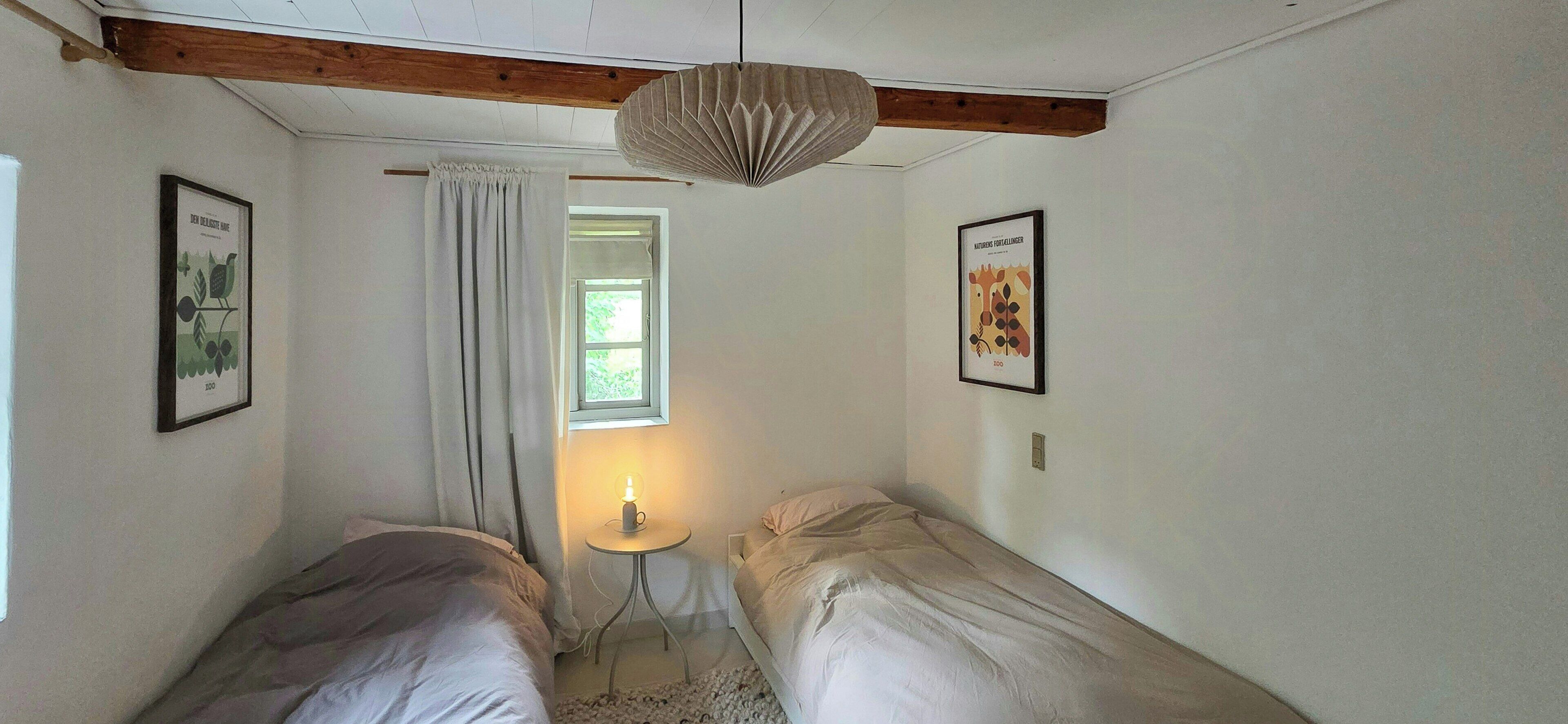 Een slaapkamer met twee eenpersoonsbedden, een raam met gordijn, een hanglamp en twee prestaties in lijsten aan de wanden.