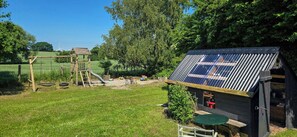 A wooden play structure with a slide and swings, a small shed with a solar panel roof, and a grassy yard.