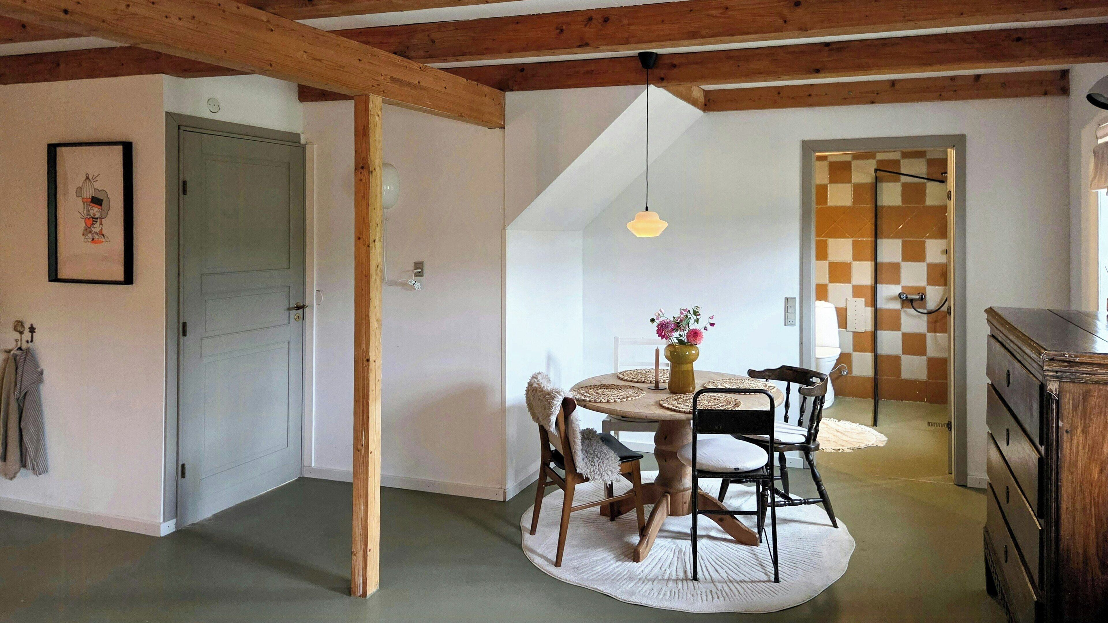 A dining area with a round table, chairs, a vase with flowers, and a hanging light fixture.