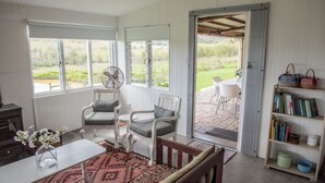 Una habitación con una mesa de comedor, dos sillas, un ventilador, una estantería y vistas al exterior.