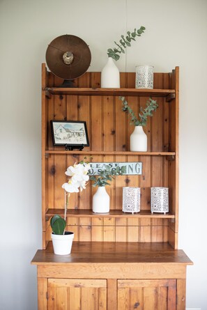 Een houten plank met diverse decoratieve items, waaronder een ingelijst beeld, een witte vaas met groene bladeren, en een bord waarop staat 'LEASE SOON'.