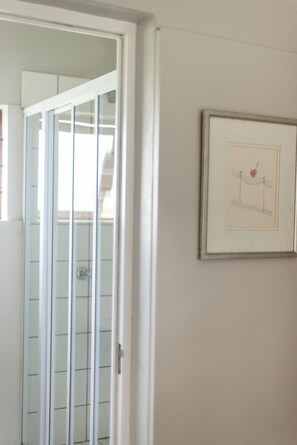 Een kamer met een deur die uitkomt op een balkon, een lijst met een afbeelding aan de muur, en een betegelde vloer.