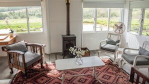 Une pièce chaleureuse avec un poêle à bois, deux fauteuils, une table et une vue sur l’extérieur.