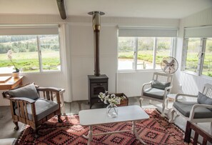 Een gezellige kamer met een houtkachel, twee stoelen, een tafel en uitzicht op de natuur.