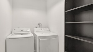 A laundry room with two white washing machines and a shelf unit.