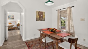 A dining area with a wooden table, chairs, a fruit bowl, and a painting on the wall.