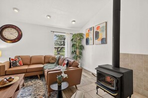 A living room with a sofa, a coffee table, a fireplace, and a clock on the wall. - Dripping Springs The Wrangler | *NEW* Hill Country Escape (Dripping Springs)