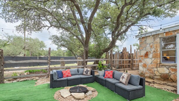 An outdoor seating area with two dark-colored sofas, a fire pit, and a stone wall.