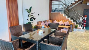 A modern hotel lobby with a glass-top table, wicker chairs, a sofa with cushions, a potted plant, and a staircase with a railing. - The SkyLine Hotel (Bhedetar)
