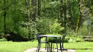 A table and chairs set in a grassy area surrounded by a dense forest.