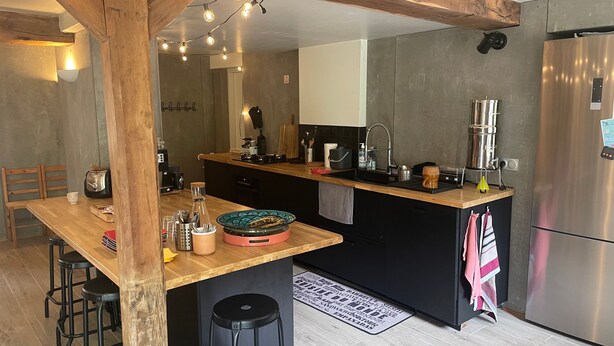 A modern kitchen with a wooden island, bar stools, a stainless steel refrigerator, and a built-in oven.