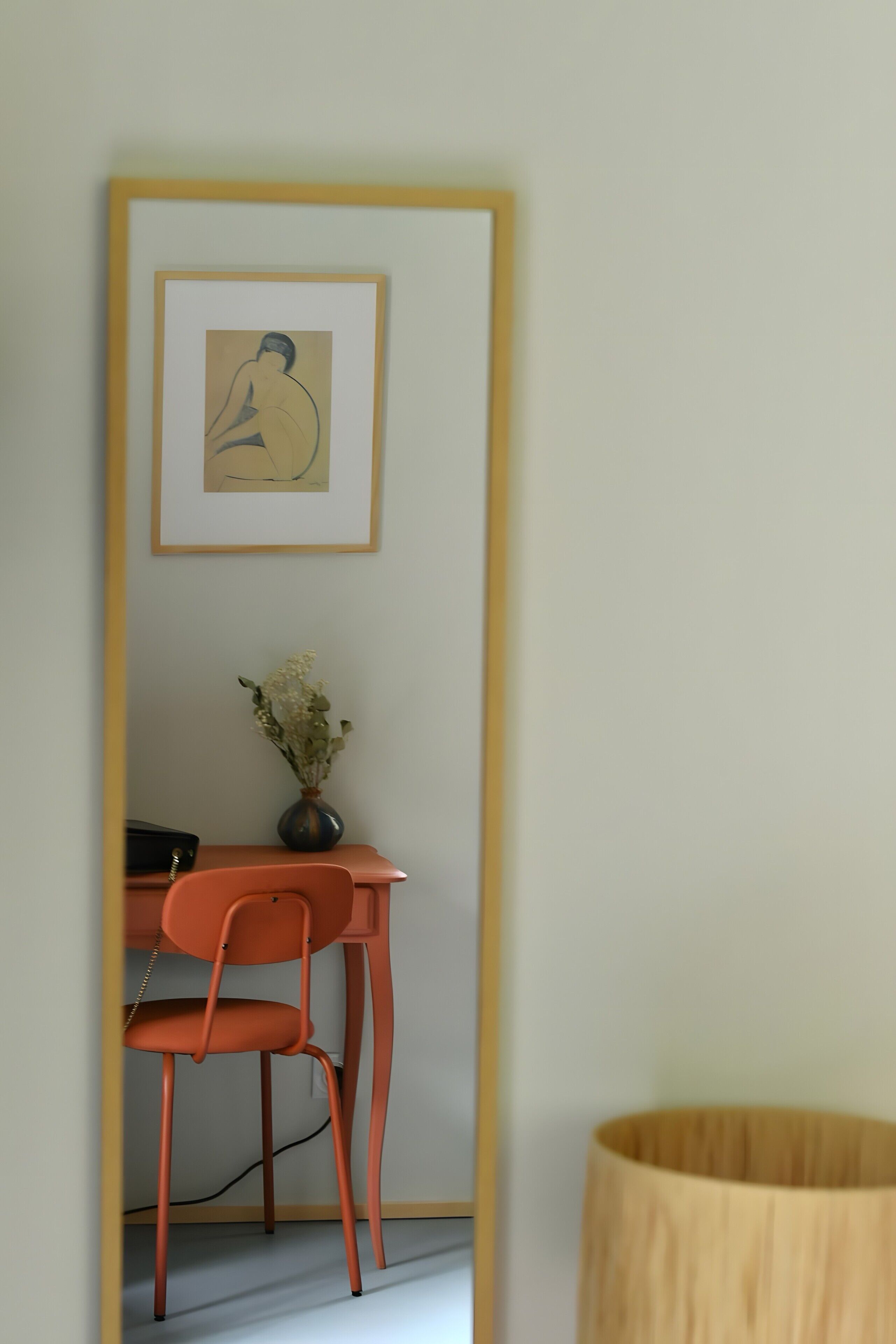 Een kamer met een bureau, stoel, kunstwerk in een lijst, een vaas met bloemen en een lamp.