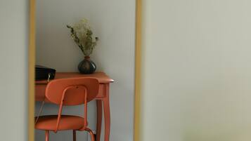 Een kamer met een bureau, stoel, kunstwerk in een lijst, een vaas met bloemen en een lamp.