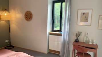 A bedroom with a bed, a desk, a chair, a window with curtains, a radiator, and wall decorations.