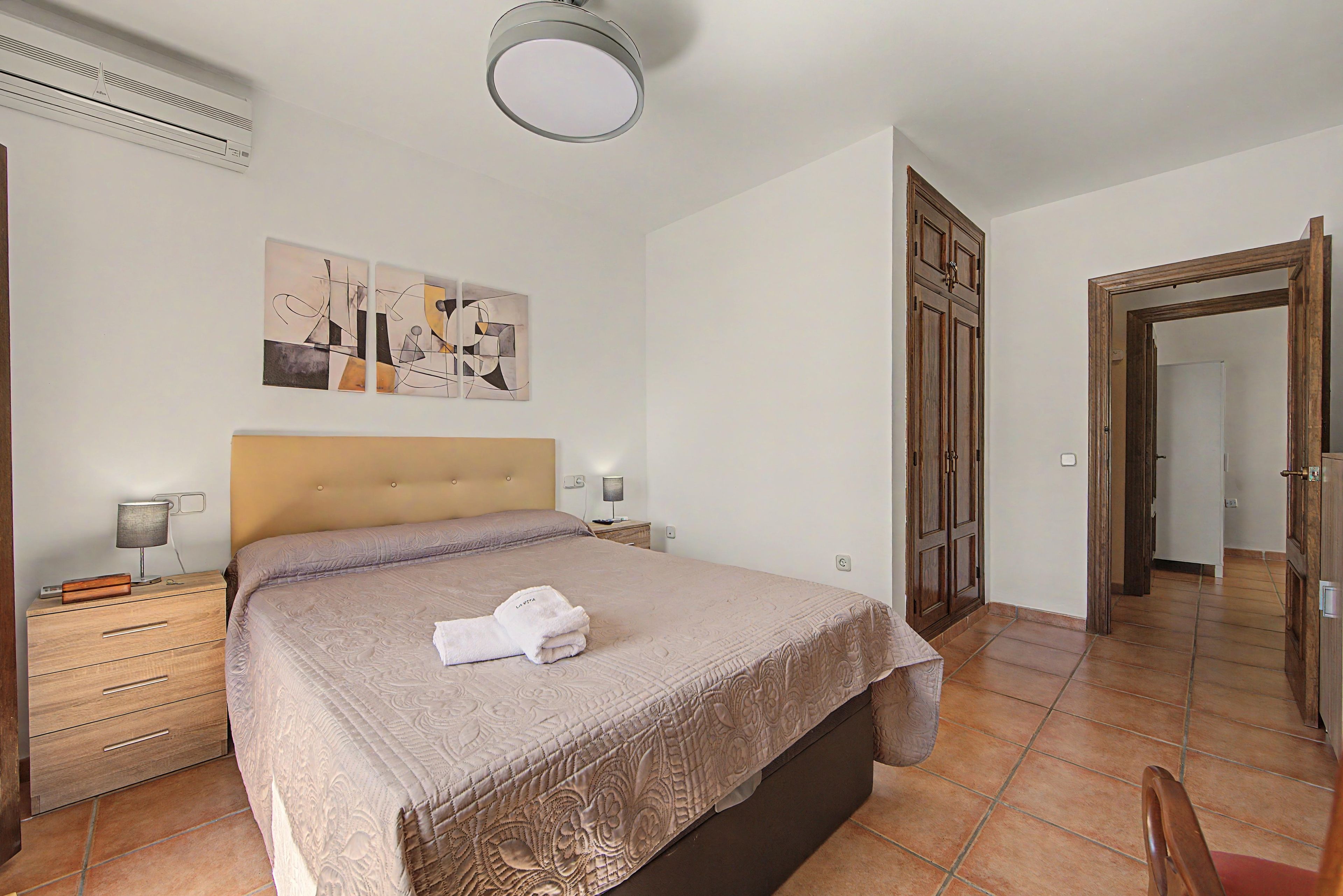 Ein Schlafzimmer mit einem Bett, einem Nachttisch, einer Lampe, einem Gemälde und einem Holzschrank.
