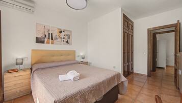A bedroom with a bed, a nightstand, a lamp, a painting, and a wooden wardrobe.