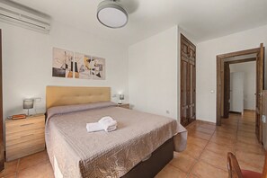 A bedroom with a bed, a nightstand, a lamp, a painting, and a wooden wardrobe. - Country House 'La Pita Casa Rural' with Mountain View, Wi-Fi and Air Conditioning (Felix)