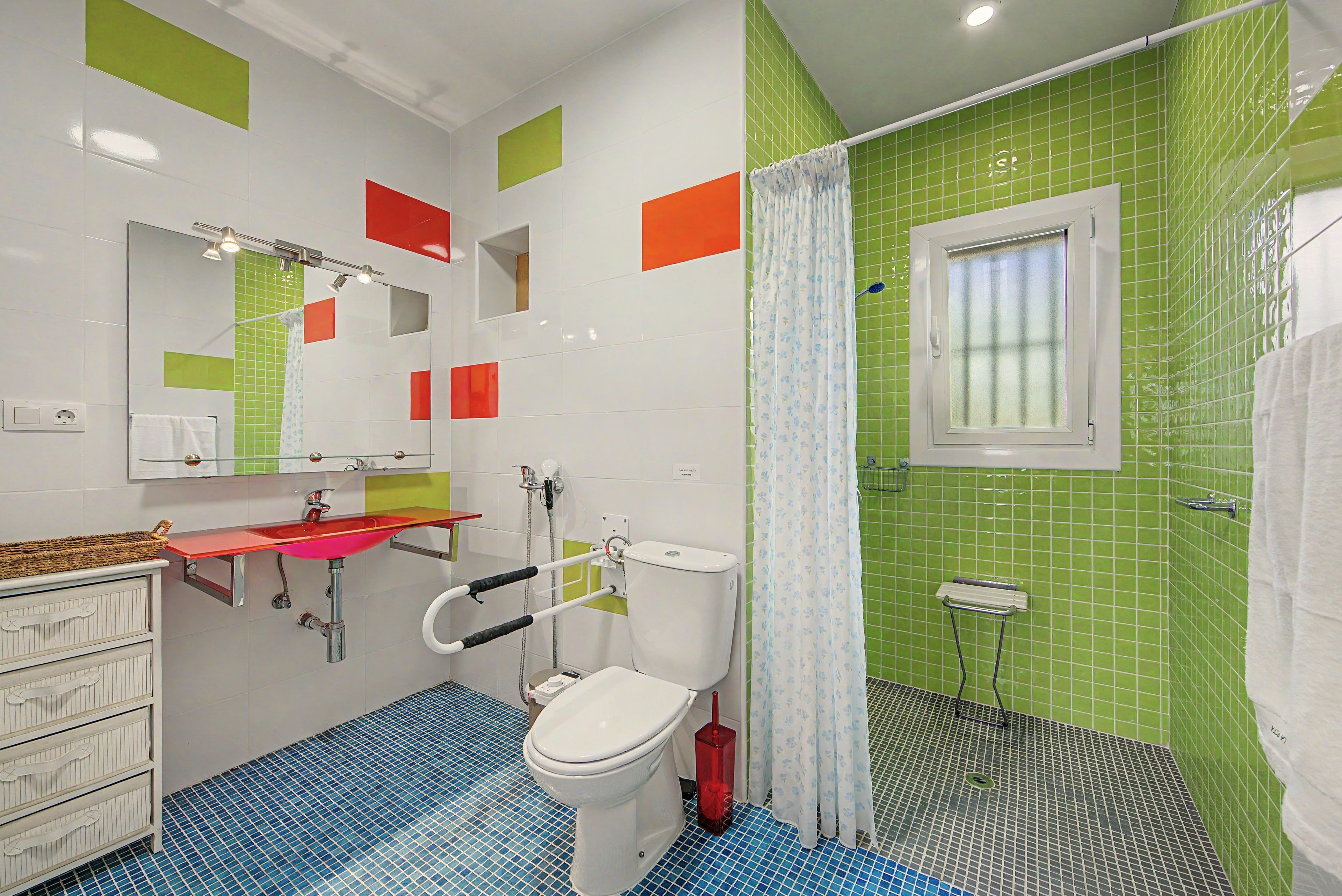 Ein Badezimmer mit einer weißen Toilette, einem roten Waschbecken und einer Duschkabine mit einer grün gefliesten Wand.
