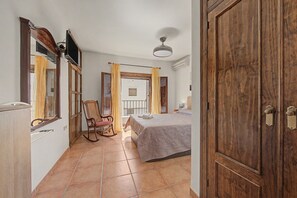 A bedroom with a bed, a rocking chair, a window with curtains, and a wooden wardrobe. - Country House 'La Pita Casa Rural' with Mountain View, Wi-Fi and Air Conditioning (Felix)