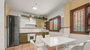 Una cocina con una mesa de comedor y sillas, un refrigerador, un horno y una ventana con rejas.