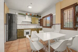 Una cucina con tavolo e sedie, un frigorifero, un forno e una finestra con sbarre.