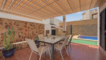 An outdoor patio with a table and chairs, a stone wall, a cactus, and a swimming pool.