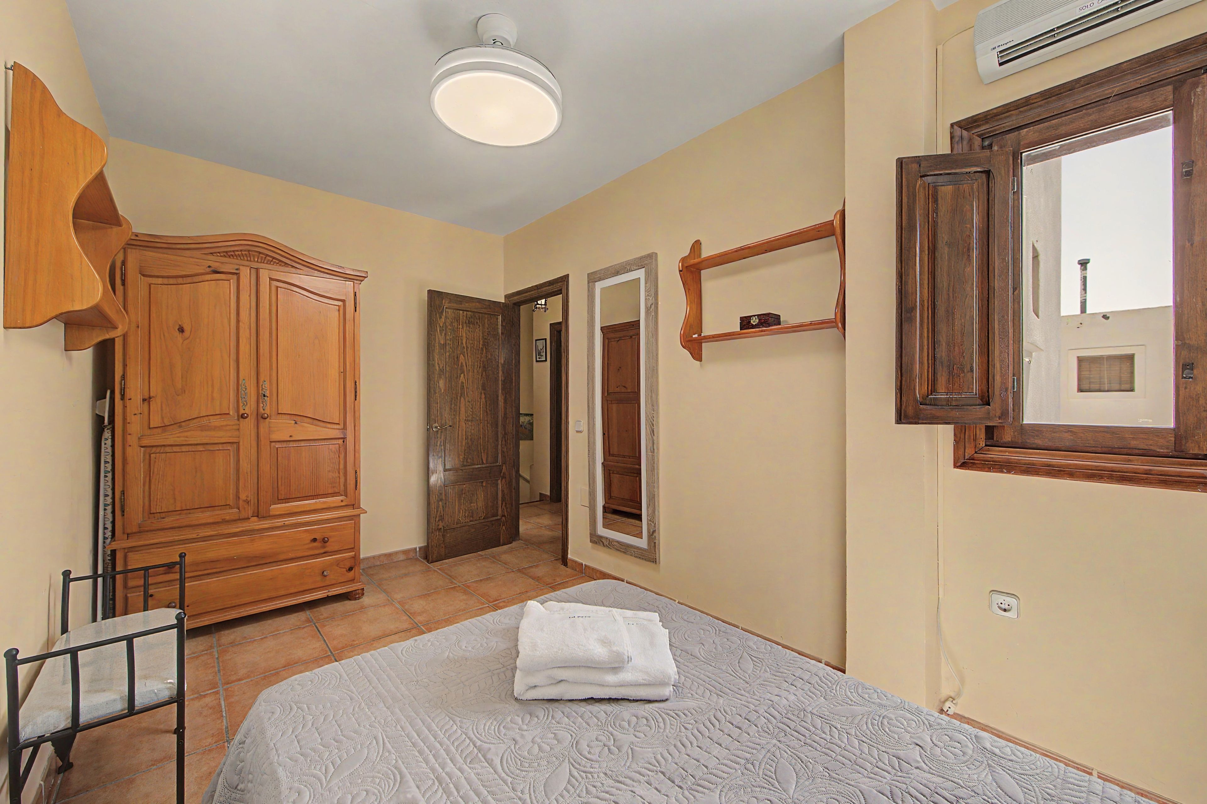 A bedroom with a bed, a wardrobe, a mirror, and a window.