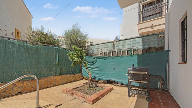 Patio trasero residencial con piscina, una parrilla y un árbol pequeño.