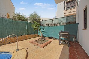 Patio trasero residencial con piscina, una parrilla y un árbol pequeño.