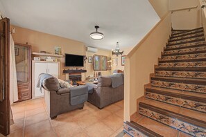 A living room with a fireplace, a television, and a staircase with decorative tiles. - Country House 'La Pita Casa Rural' with Mountain View, Wi-Fi and Air Conditioning (Felix)