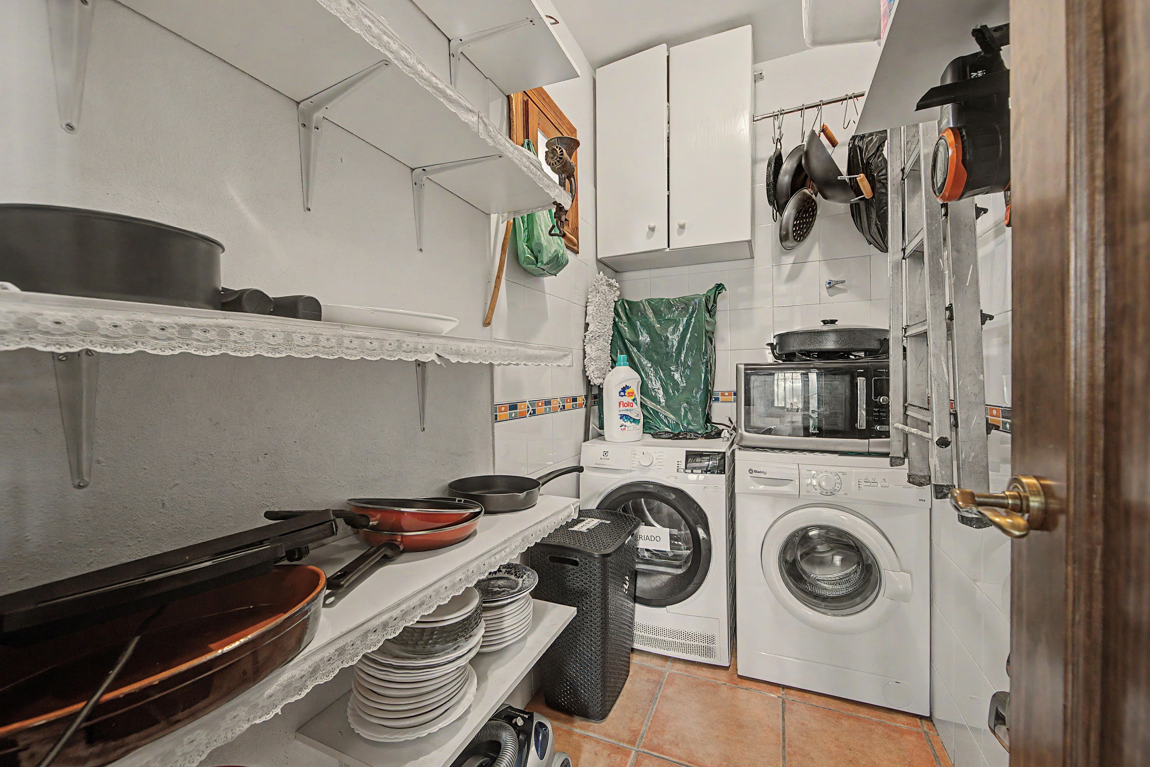 Een kleine keuken met een wasmachine, een fornuis en diverse keukengerei.