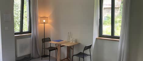 Una habitación con cama, dos sillones, una mesa, una lámpara y dos ventanas con cortinas.