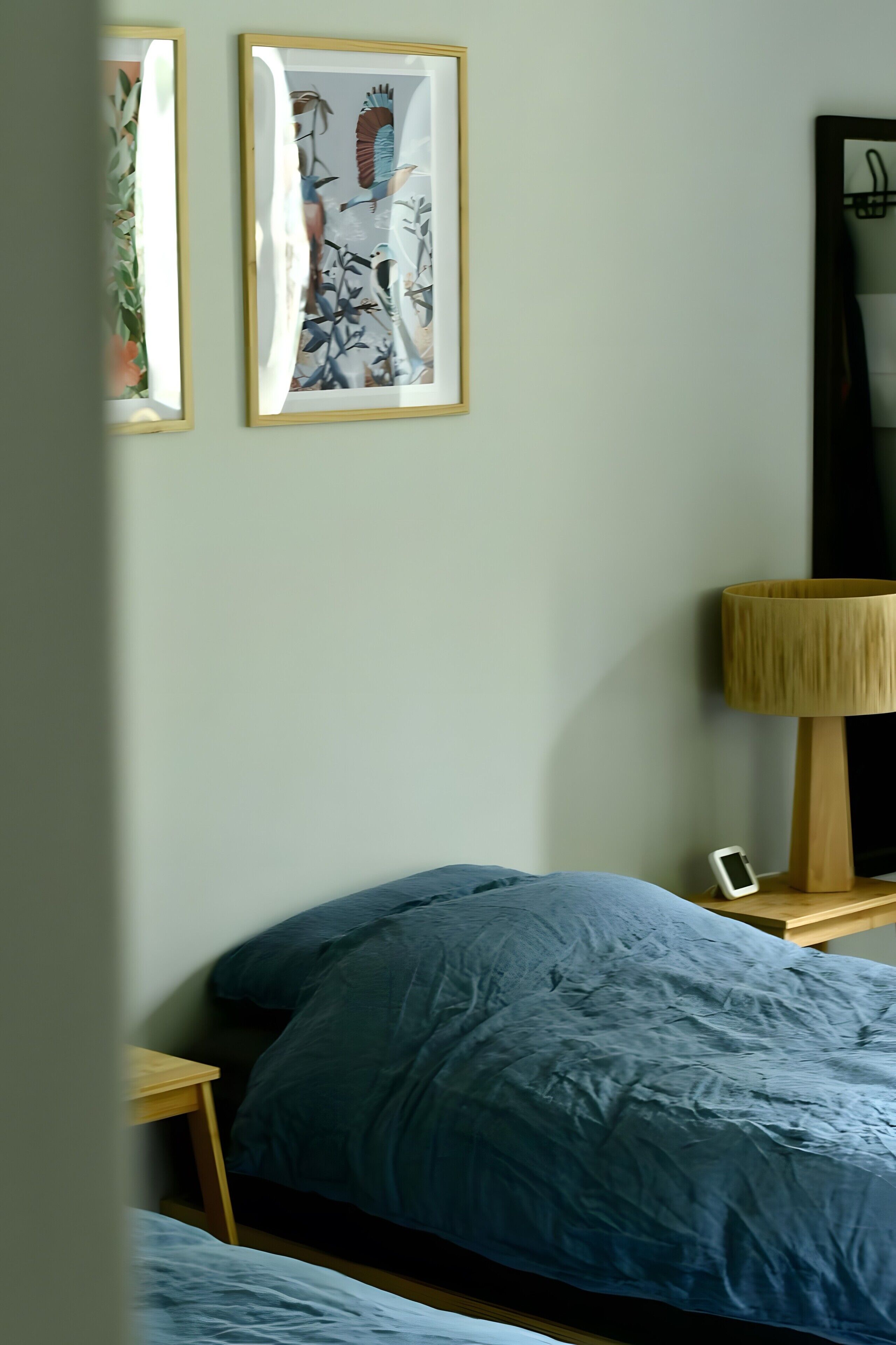Quarto com uma cama, mesa de cabeceira, luminária e duas fotografias emolduradas na parede.