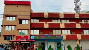 A multi-story building with a red and beige facade, a visible sign for a hotel, and a parked auto-rickshaw in front. - Shivmurti Grand  (Haridwar)