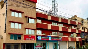 A multi-story hotel with a red and beige facade, a visible entrance, and a parking area with motorcycles. - Shivmurti Grand  (Haridwar)