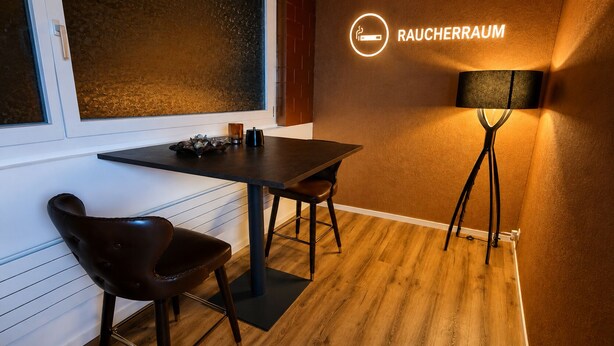 Una habitación con una mesa, dos sillas, una lámpara y un letrero que dice 'RAUCHERRAUM'.