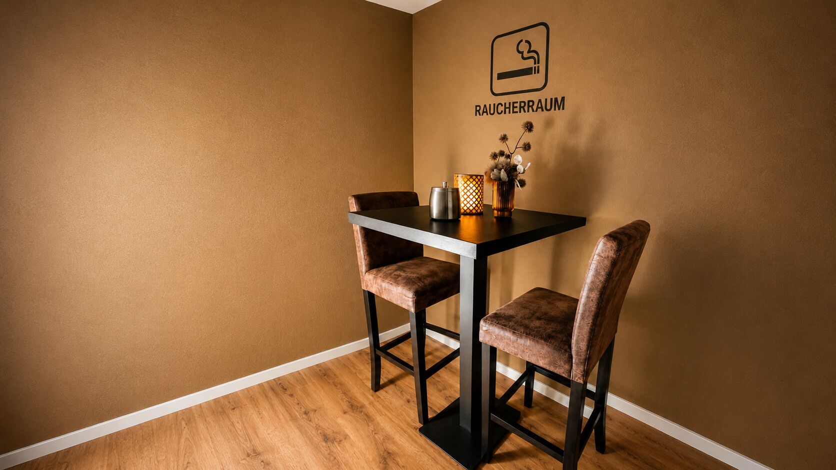 Un coin repas avec une table et deux chaises, un panneau fixé au mur indiquant « RAUCHERRAUM » (salle de fumeurs), et un vase décoratif contenant des fleurs séchées.