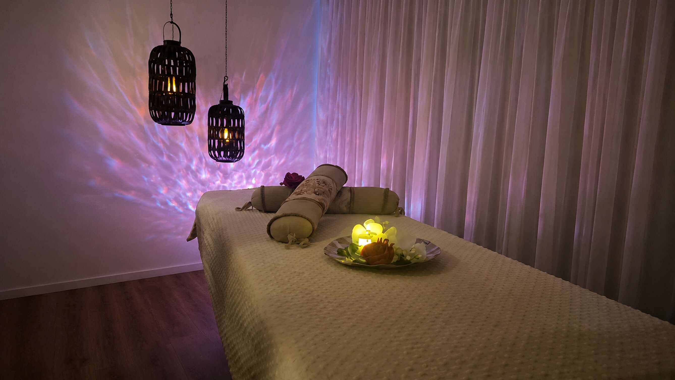A massage table with a white cover, two candles, and a decorative plate with flowers.