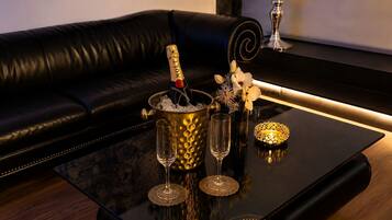 Ein schwarzes Ledersofa, ein goldener Eimer für Eis mit einer Flasche, zwei Gläser und eine dekorative Schale auf einem reflektierenden schwarzen Tisch.
