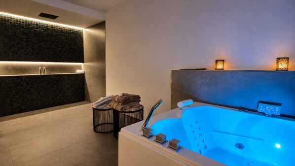 A modern spa room with a heated bathtub, a towel stack, and ambient lighting.