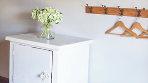 A white cabinet with a vase of flowers, wooden wall hangers, and a wooden ceiling.