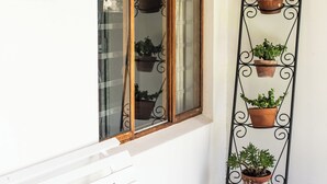 A white bench outside a building with a window and a metal plant stand with potted plants.