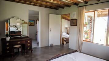 A bedroom with a wooden bed, a dresser with drawers, a mirror, and a door leading to another room.