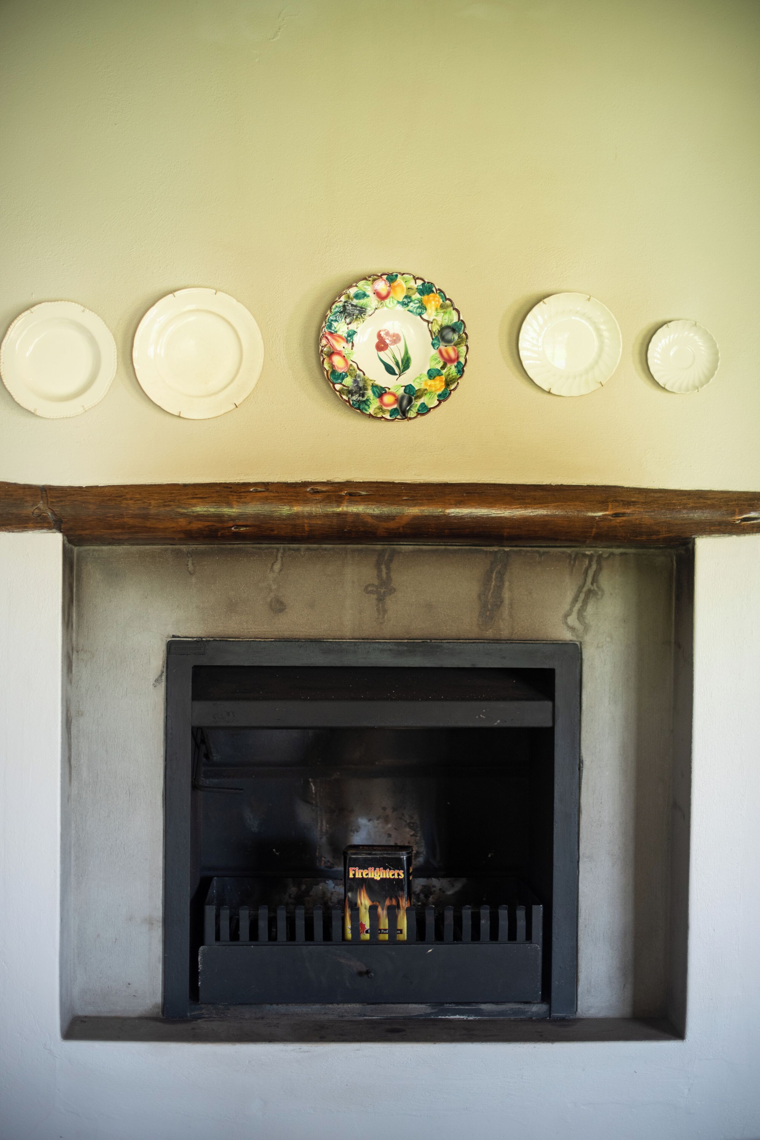 Una chimenea con un repisa superior que exhibe tres platos blancos y uno con un diseño de frutas.