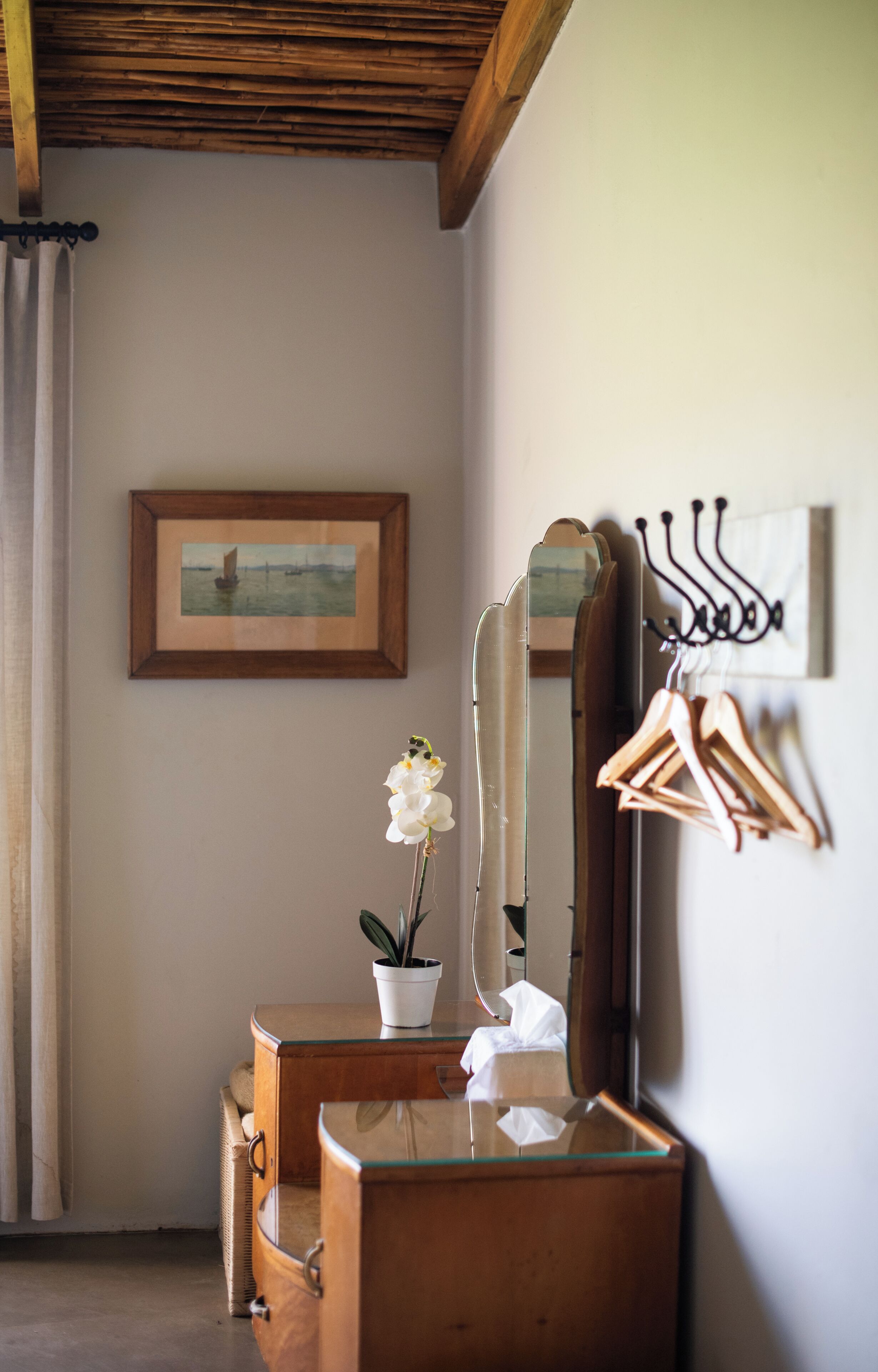 Une pièce avec une commode en bois, un miroir, un tableau encadré au mur et un pot d’orchidée.
