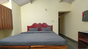 A single bed with a wooden headboard and grey bedding in a room with cream walls and a sloped ceiling. - Mistora Valley (Ooty)