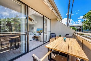 A modern living room with a large window, a wooden table, and a view of the outdoors. - Beautiful Ocean View 2 Bedroom Condo 1 Min Walk to Beach! (Kihei)