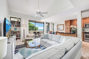 Ein modernes Wohnzimmer mit Sofa, Couchtisch und Fernseher. Ein Balkon bietet Blick auf den Ozean.
