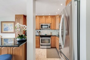 A modern kitchen with stainless steel appliances, wooden cabinets, and a tiled backsplash. - Beautiful Ocean View 2 Bedroom Condo 1 Min Walk to Beach! (Kihei)